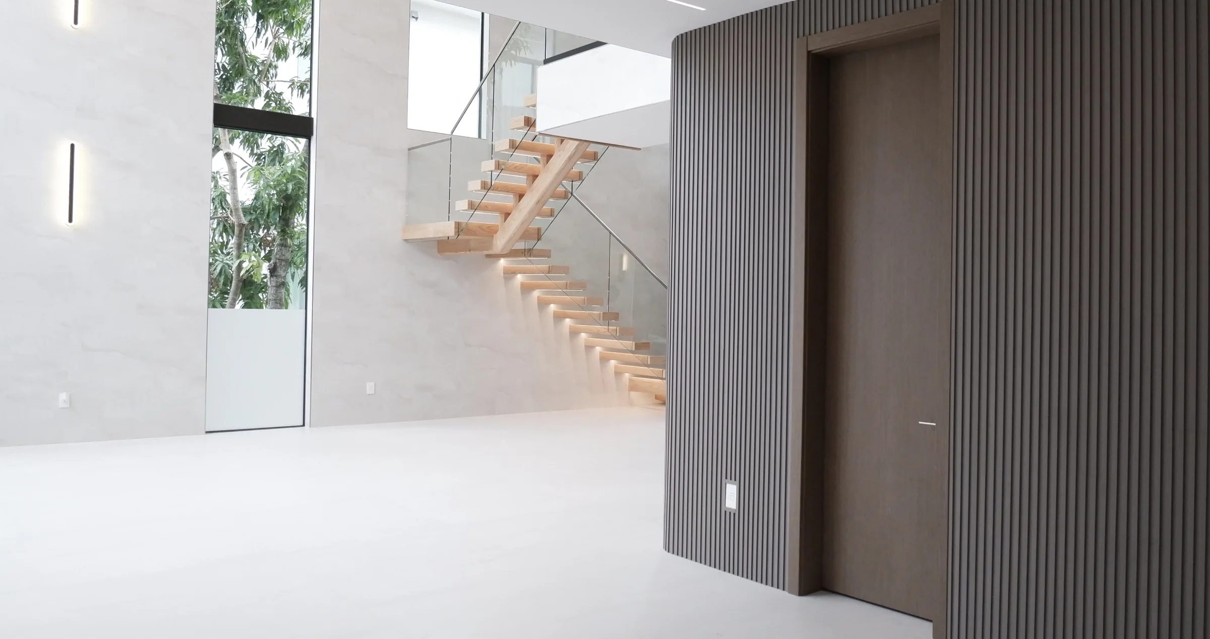 Slatted wood wall with concealed door beside a floating staircase